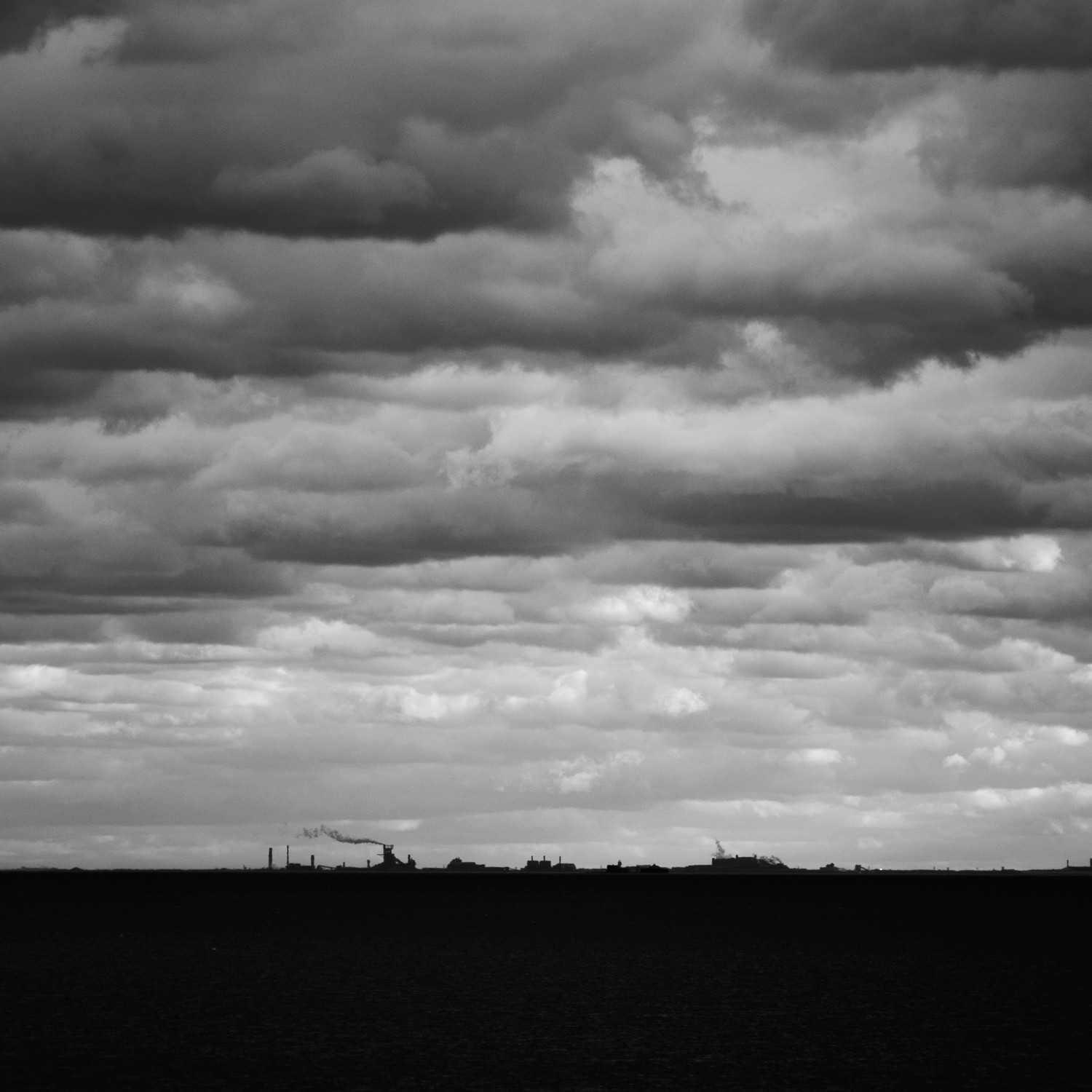 Distant industrial buildings silhouetted against a cloudy sky